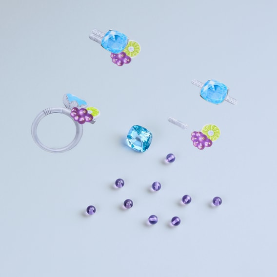 Composition of colorful costume jewellery, including a ring and earring elements with blue stones, purple and green floral motifs, and purple beads, on a light background