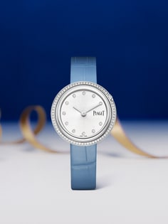Piaget Possession watch with a round white gold case, a bezel set with diamonds, and a silver dial featuring diamond hour markers. It has two silver hands and is paired with a light blue alligator leather strap.